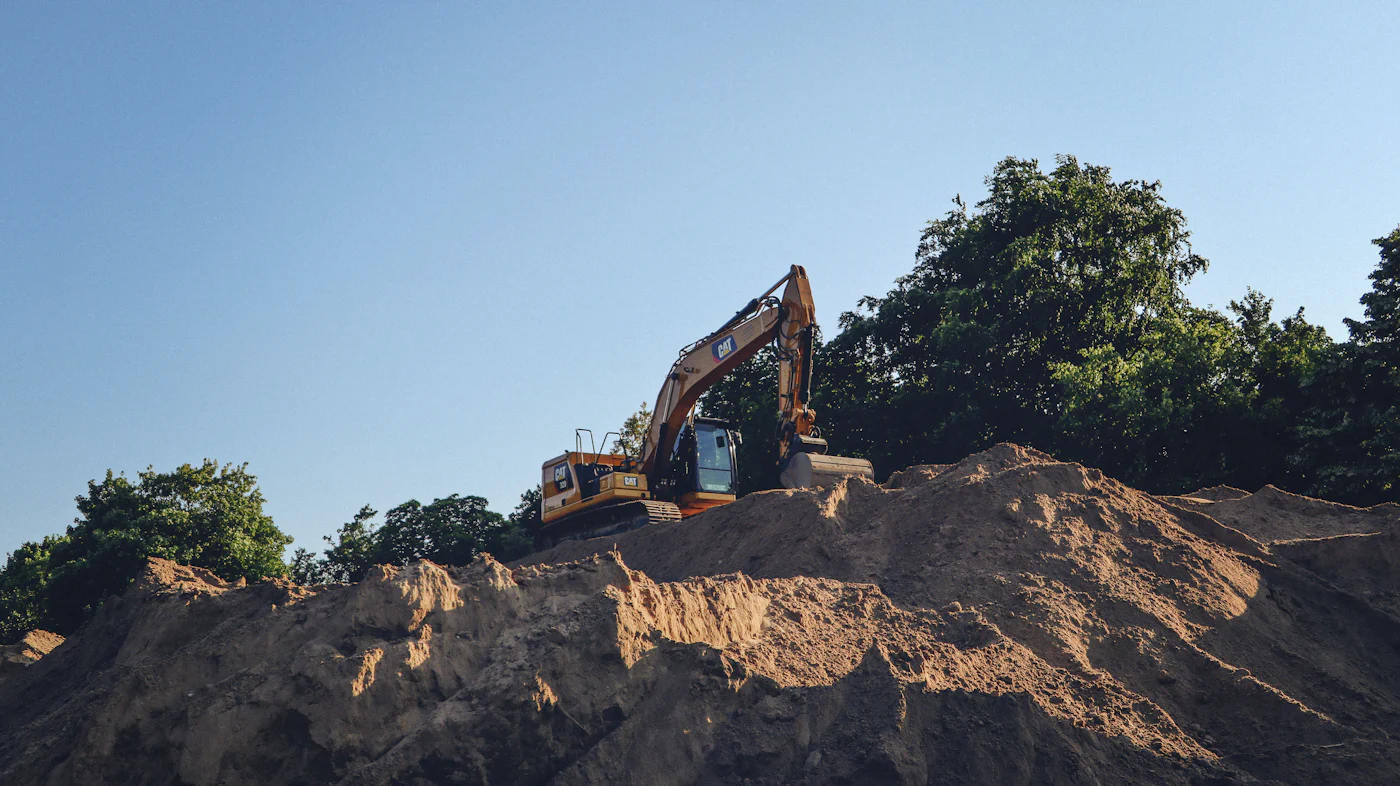 Tracked excavator working on top of a large dirt pile against a clear sky