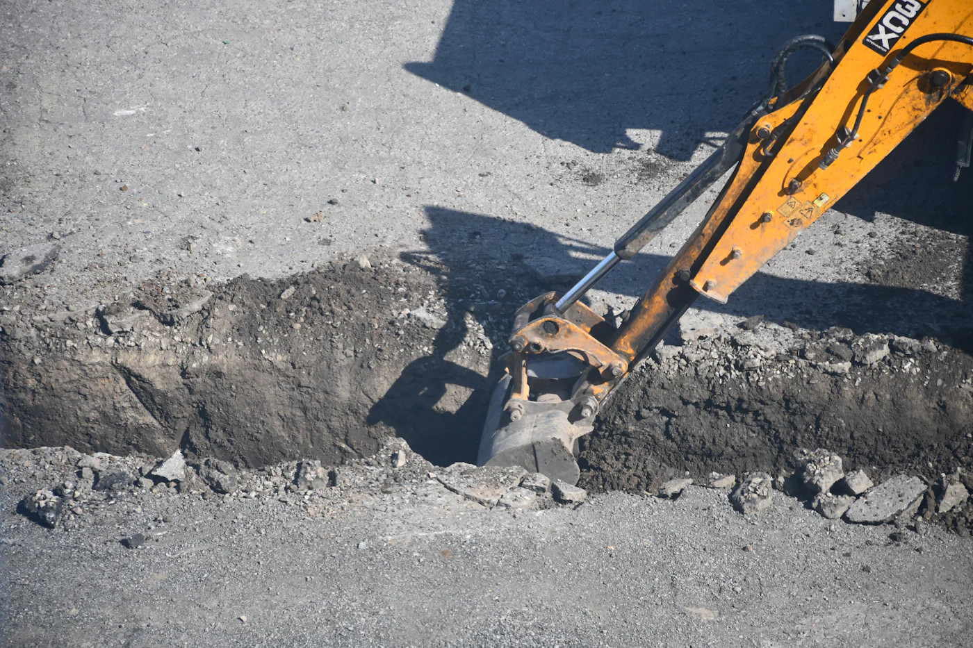 Excavator opening a trench along a roadside with utility lines exposed